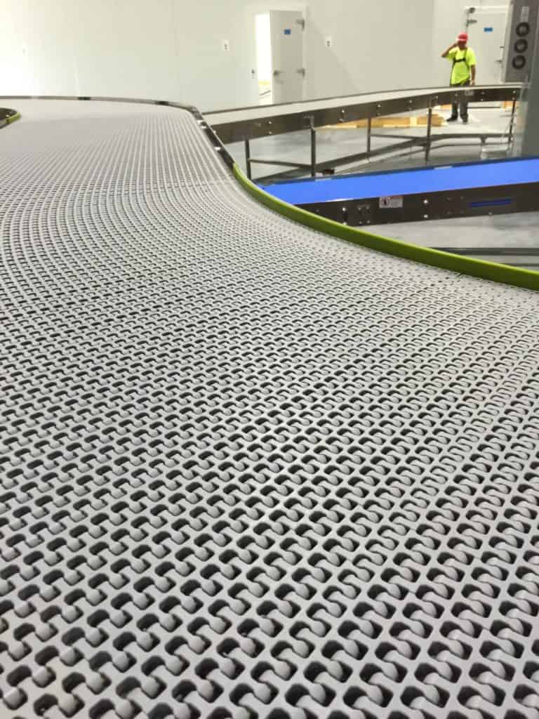 Wire mesh belt conveyor curving through a plant with an operator working behind it